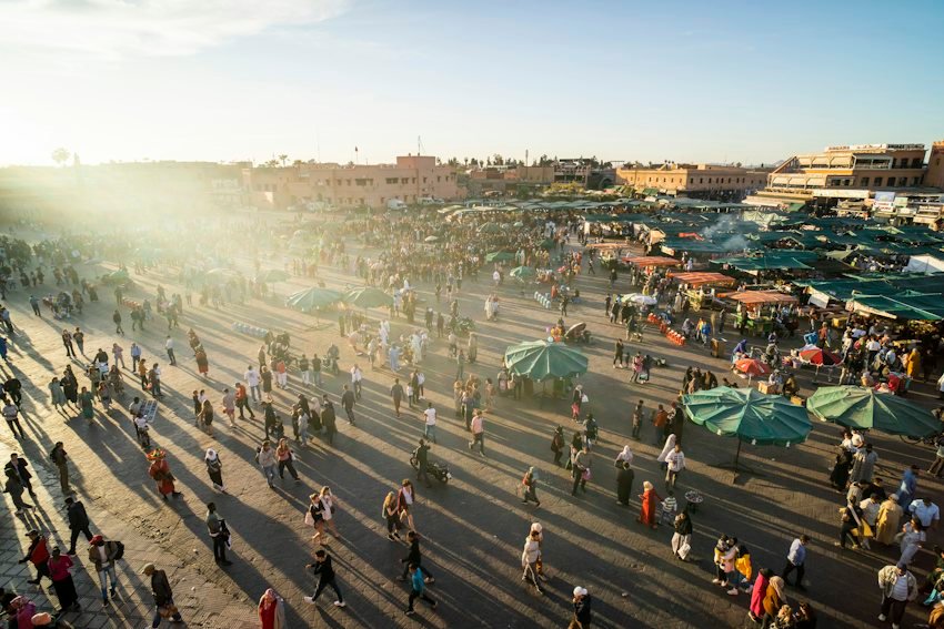 La plaza Jemaa el-Fna de Marrakech con puestos de mercado y visitantes antes del atardecer.
